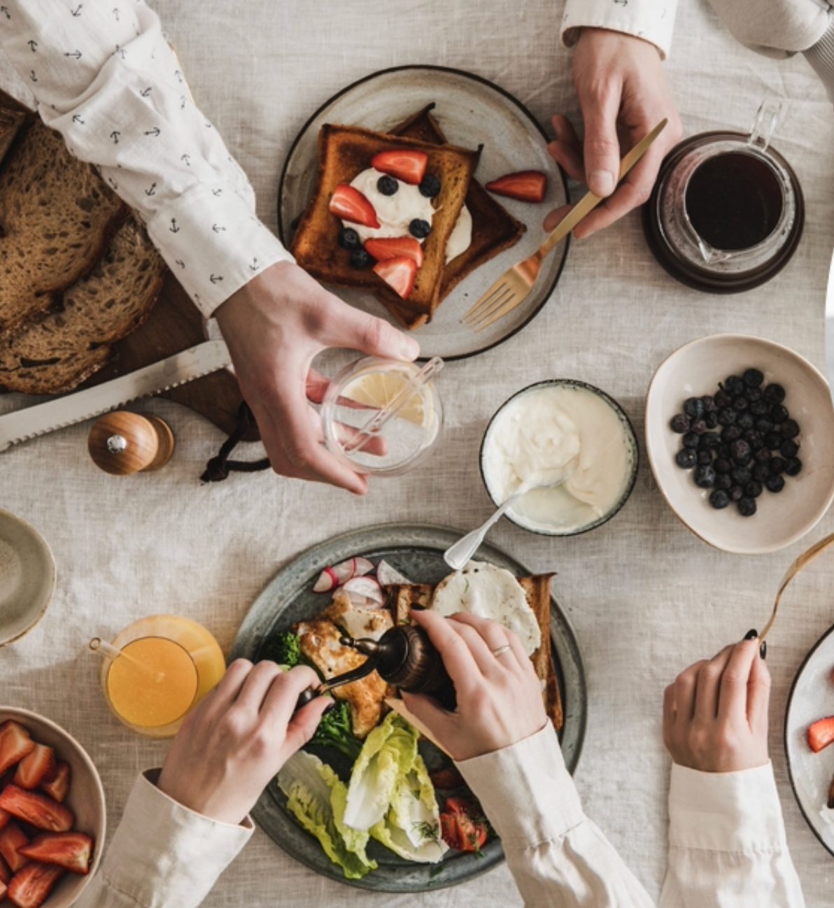 Una mesa de desayuno mediterráneo vista desde arriba — tostada integral, yogur, frutos rojos, huevos y aceite de oliva